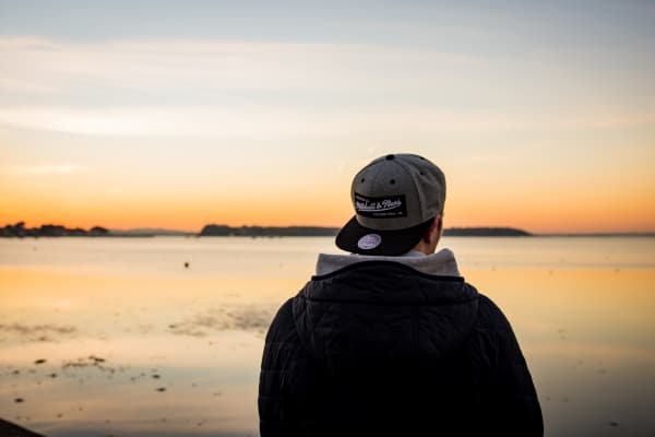 Portrait of a longing pensive teenager sitting on the beach looking away at the horizon in the morning